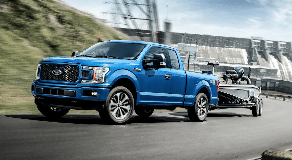 A blue 2019 Ford F150 tows a boat with a dam in the back