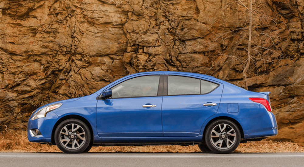 A blue 2015 Nissan Versa is shown in front of rock face. It is a good example for slowly depreciating used cars.