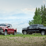 Two 2019 Chevy Silverados are shown in front of pines and distant mountains. One is red and the other black.
