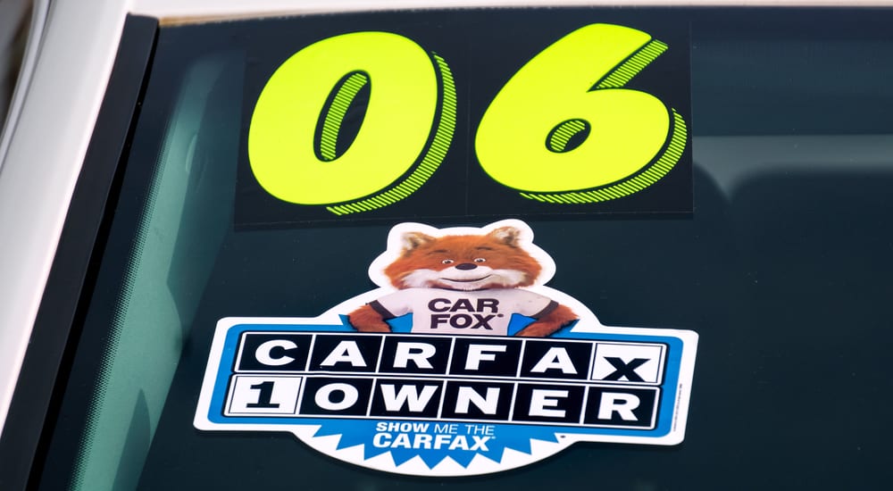 A Carfax "one owner" and "06" year sticker are on a car windshield. 