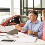 Couple with a salesman making a deal in a car showroom