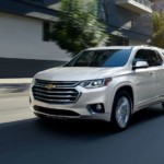 A white 2019 Chevy Traverse is driving through a sunny city.
