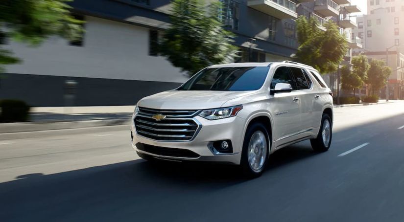 A white 2019 Chevy Traverse is driving through a sunny city.