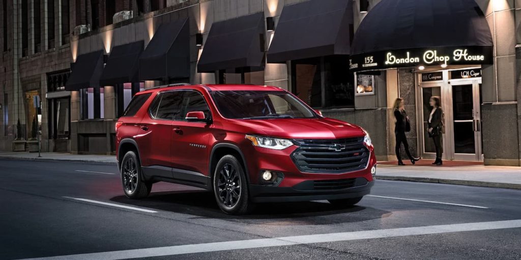 A red 2019 Chevy Traverse with black trim is driving through a city at night.