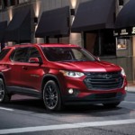 A red 2019 Chevy Traverse with black trim is driving through a city at night.