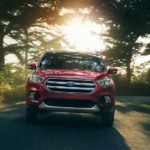 A red 2019 Ford Escape is driving with sun shining through the trees.