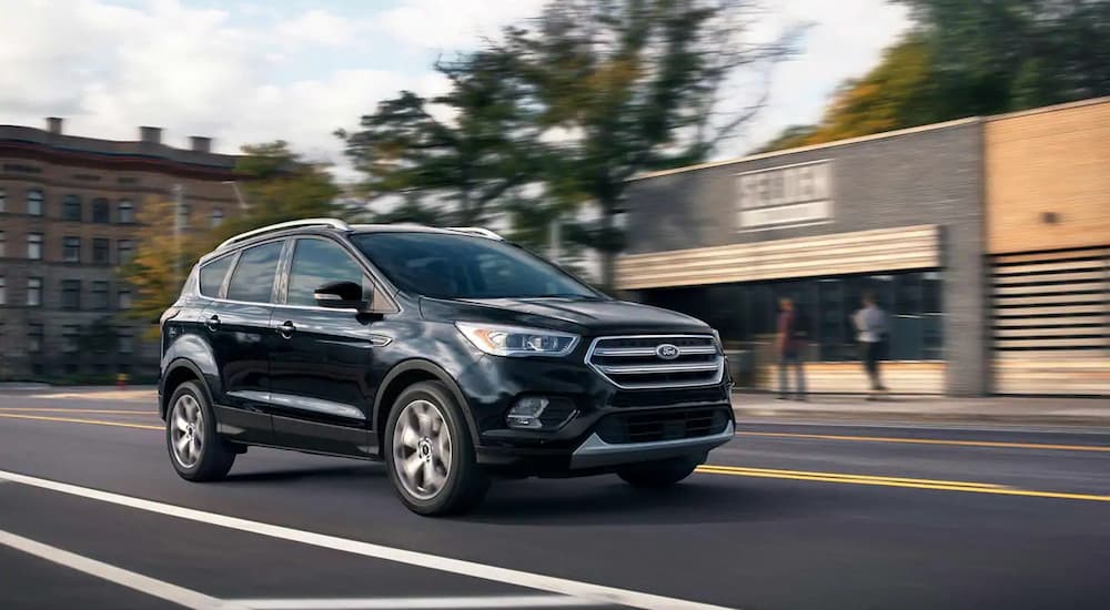 A black 2019 Ford Escape Titanium is driving downtown. Check out trim levels when comparing the 2019 Ford Escape VS 2019 Nissan Rogue.