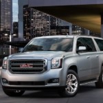 A silver 2019 GMC Yukon XL is parked at a modern building in a city at night.