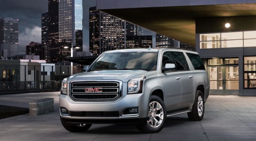 A silver 2019 GMC Yukon XL is parked at a modern building in a city at night.