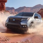 A silver 2019 Honda Passport is splashing through a puddle with red rocks desert around it.