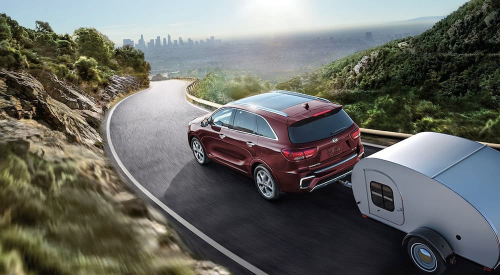 A red 2019 Kia Sorento is towing a small camper on a narrow road.