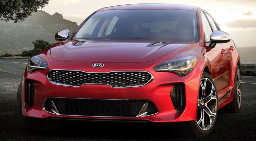 A red 2019 Kia Stinger is parked with a winding road and a bay behind it.