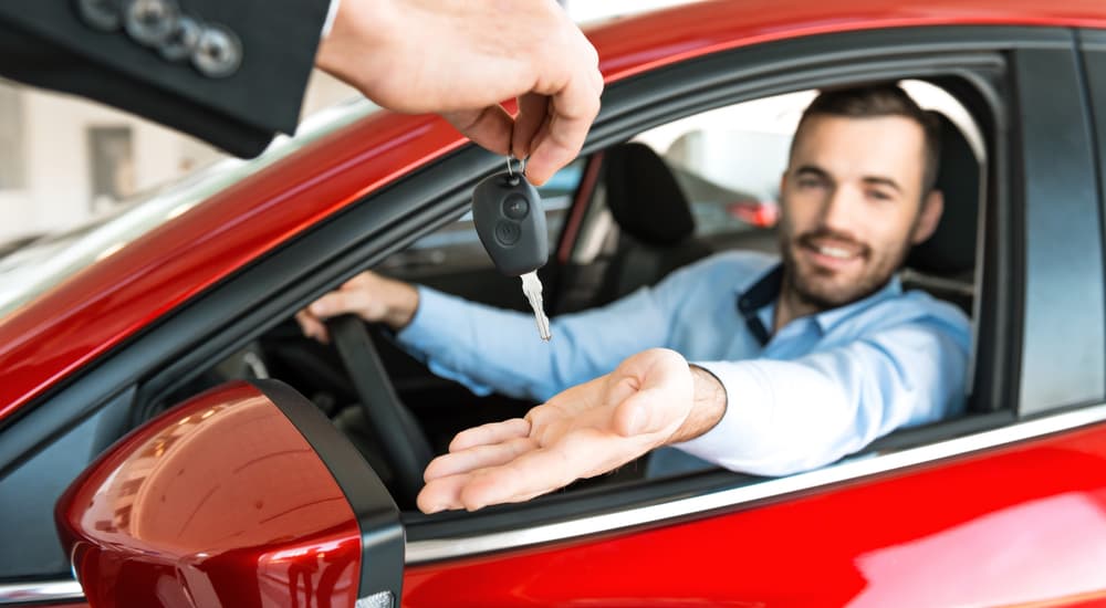 A dealer is handing a happy man the keys to his new red car. He got his car with the help of no credit car loans.