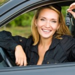 A woman is smiling and holding her keys while sitting in her new car.
