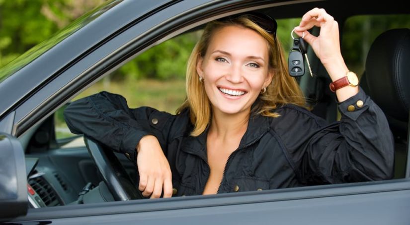 A woman is smiling and holding her keys while sitting in her new car.
