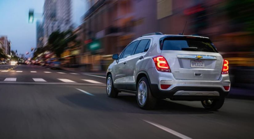 A white 2019 Chevy Trax is driving through a city at dusk.