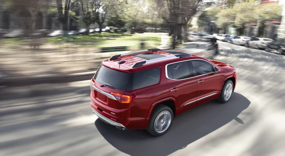 A red 2019 GMC Acadia is driving away around a corner in a downtown. Check out performance when comparing the 2019 GMC Acadia vs 2019 Honda Pilot.
