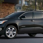 A black 2019 GMC Acadia is parked in front of buildings.