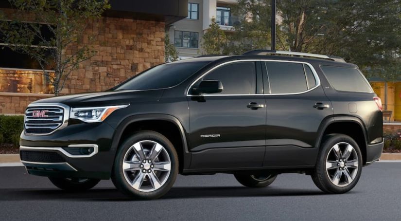 A black 2019 GMC Acadia is parked in front of buildings.