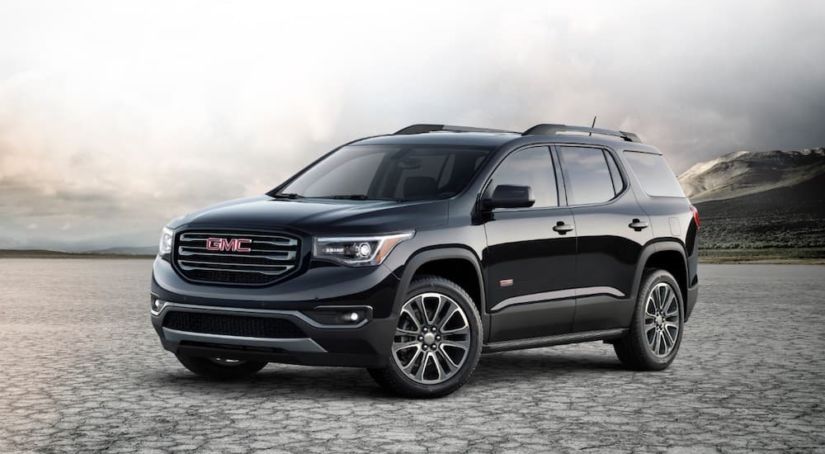 A black 2019 GMC Acadia is parked on cracked ground in front of misty mountains.