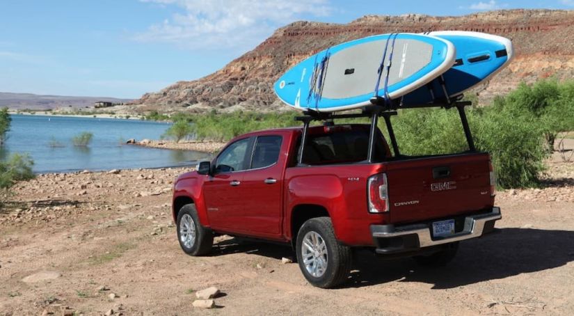 A red 2019 GMC Canyon is parked at a lake with paddle boards on the bed rack.