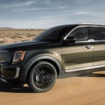 A green 2020 Kia Telluride is driving through the desert.