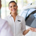 A sales woman is talking to a customer about a white SUV at a Buy Here Pay Here dealership.