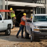 Two Chevy commercial vehicles are parked at a job site. Men are loading their trucks.