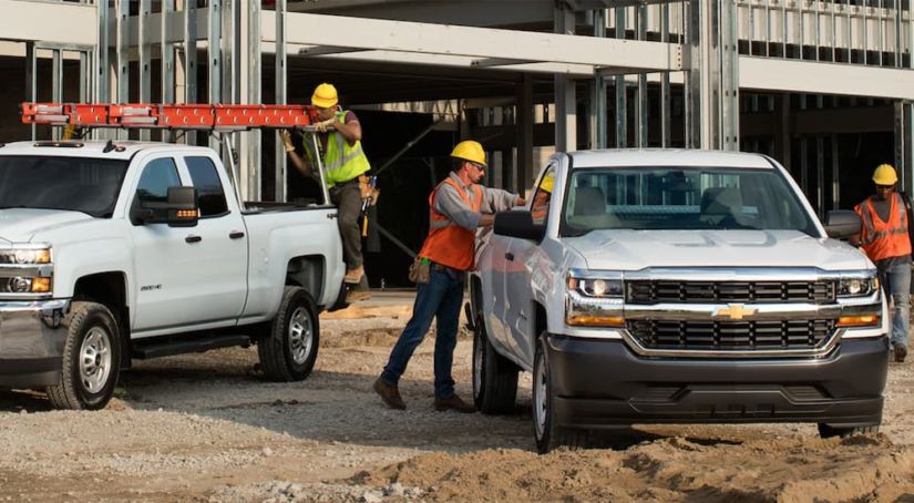 Two Chevy commercial vehicles are parked at a job site. Men are loading their trucks.