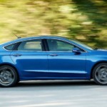 A blue 2019 Ford Fusion, purchased as a Ford Certified Pre Owned car, is driving in front of blurred trees.