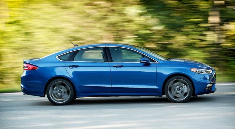 A blue 2019 Ford Fusion, purchased as a Ford Certified Pre Owned car, is driving in front of blurred trees.