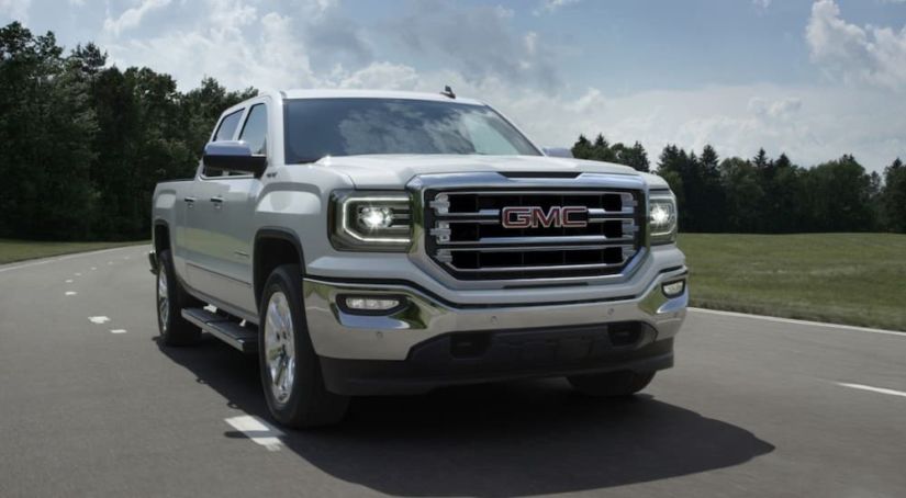 A white 2017 GMC Sierra, one of the popular used trucks for sale, is driving down the middle lane on a highway.