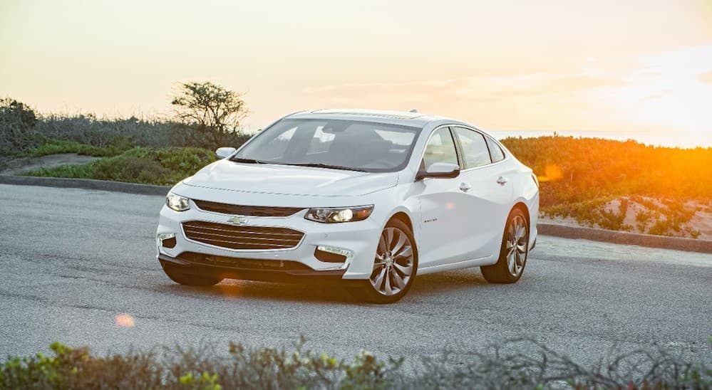 A white 2016 Chevy Malibu, popular among used cars for sale near me, is parked with a sunset behind it.