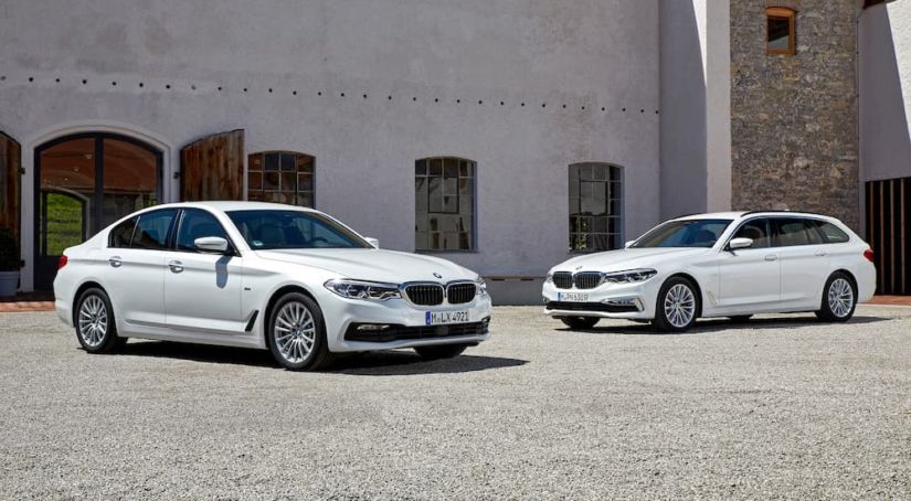 Two white 2017 BMW 5 Series are parked in front of a tan building.