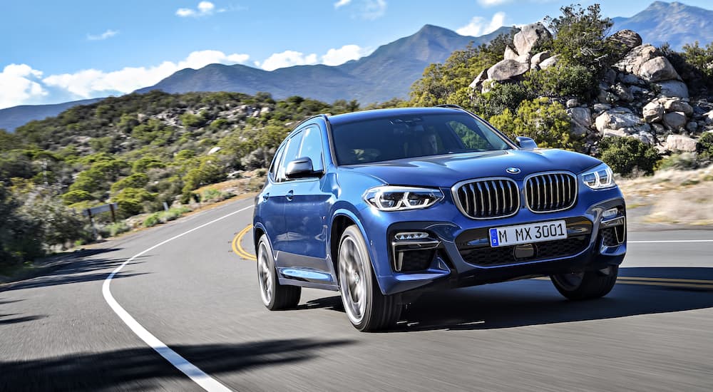 A blue 2018 BMW X3 Blue is driving in front of mountains.