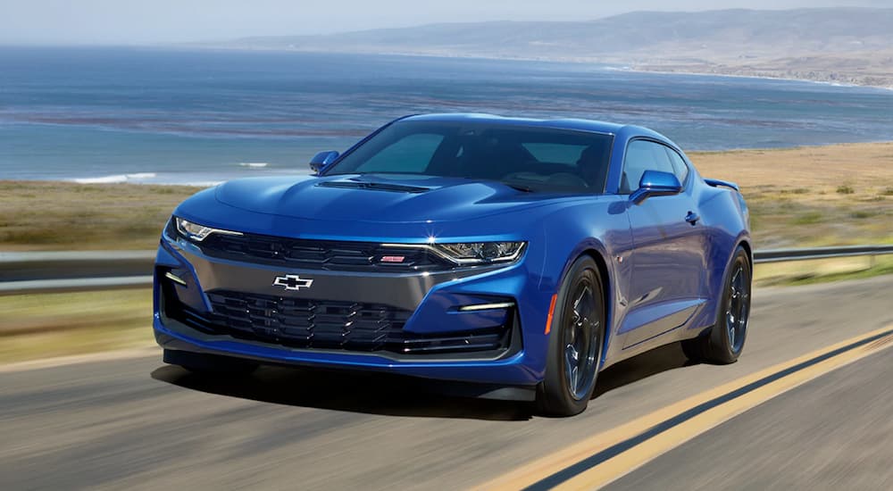 A blue 2019 Chevy Camaro, which you can find by searching 'chevy dealership near me', is driving along a beach.