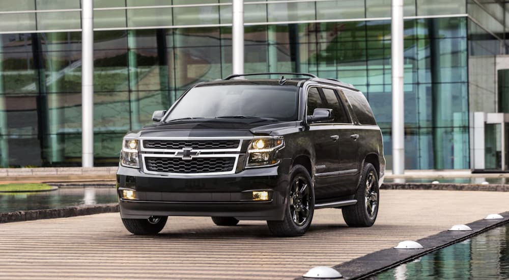 A black 2019 Chevy Suburban is parked in front of a glass building.