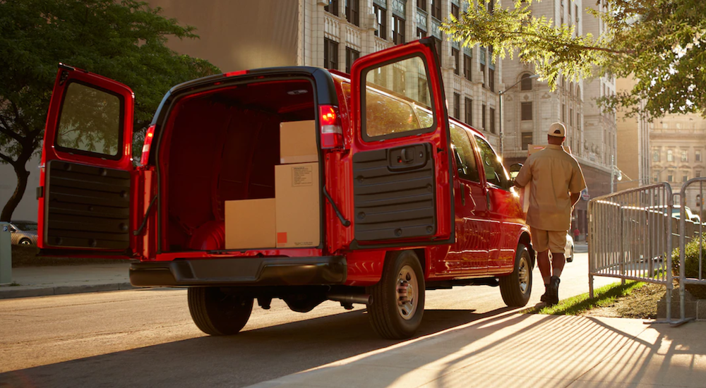 A red 2019 Chevy Cargo Van is parked in a city with a delivery worker walking away.