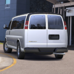 A silver 2019 Chevy Passenger Van, one of the popular Chevy vans for sale, is parked outside a building.