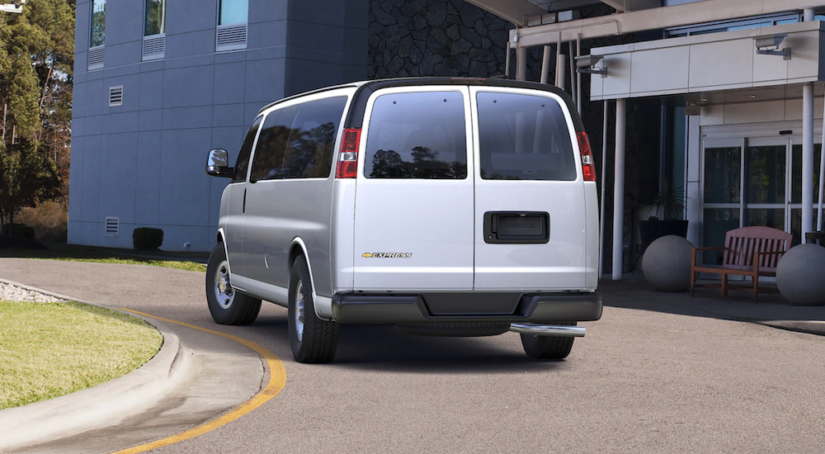 A silver 2019 Chevy Passenger Van, one of the popular Chevy vans for sale, is parked outside a building.