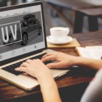 A woman is on her laptop looking at a current auto news page on SUVs.