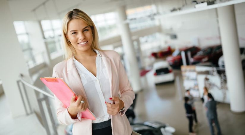 A smiling saleswoman at one of the dealerships in Nashville is standing on an upper level with cars and buyers below her.