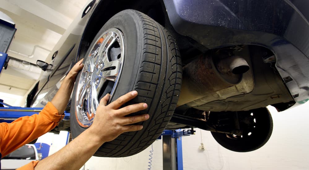 A mechanic has a car on a lift while inspecting the tires.