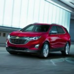 A red 2019 Chevy Equinox is driving past a lit building at night.