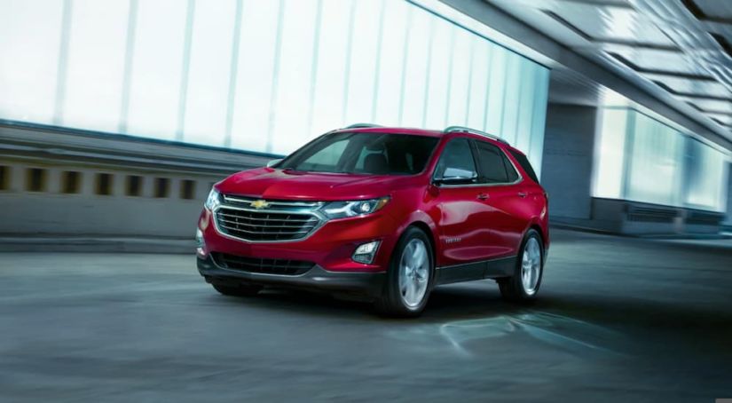 A red 2019 Chevy Equinox is driving past a lit building at night.