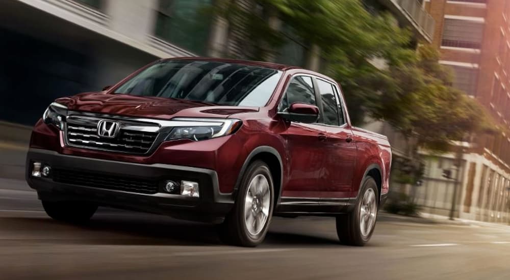 A burgundy 2019 Honda Ridgeline, which does not win when comparing the 2019 Ford Range vs 2019 Honda Ridgeline, is driving past city buildings.
