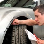 A man with a paper is inspecting the front end of his car.