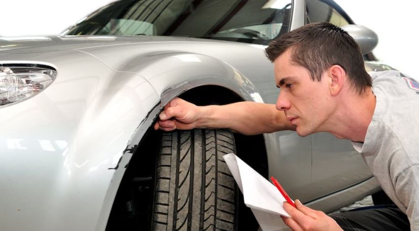 A man with a paper is inspecting the front end of his car.