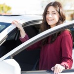 A young woman is smiling while getting into her new white car.