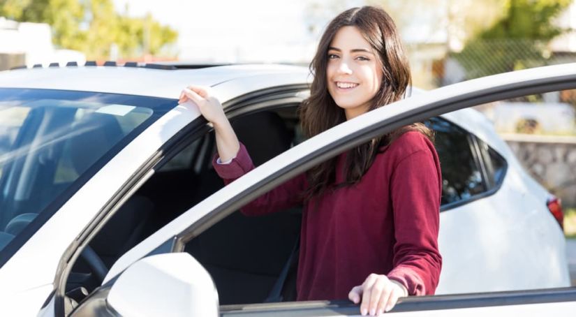 A young woman is smiling while getting into her new white car.